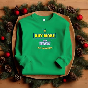 May include: A bright green sweatshirt with the text "BUY MORE" in a blue and yellow box. Below the text is the address "9000 BURBANK BOULEVARD BURBANK, CA" and the phrase "YOUR TECH PARADISE". The sweatshirt is displayed on a wooden tray with pine needles, pine cones, and red ornaments.