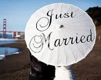 Fotografía de boda personalizada con sombrilla y letrero de accesorio: "Recién casados", sesión de fotos nupcial en la playa.