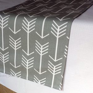 May include: A gray table runner with a white arrow pattern. The arrows are pointing in different directions.