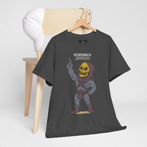 May include: Dark gray t-shirt featuring a cartoon illustration of a skeletal character with a yellow skull and purple hood. The character is pointing upwards. The text "REMEMBER YOU'RE ONLY LATE WHEN YOU SHOW UP" is above the character.