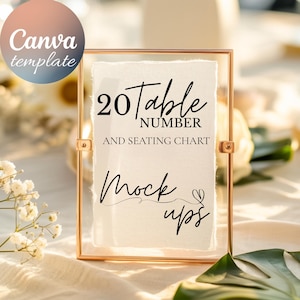 Könnte beinhalten: Ein goldfarbener gerahmter Schild mit dem Text "20 Table Number and Seating Chart Mock ups" in schwarzer Schrift. Das Schild wird auf einem Tisch mit Blumen und Grün in der Hintergrund gezeigt. Ein Canva-Vorlagenlogo befindet sich in der oberen linken Ecke.