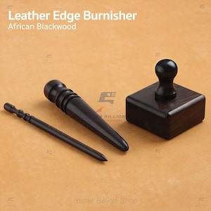 May include: A set of leather edge burnishing tools made from African Blackwood. The set includes a burnisher, a groover, and a square-shaped wooden tool with a rounded handle. The tools are dark brown and sit on a light brown surface.