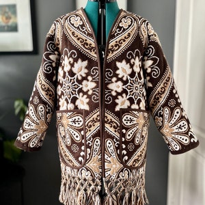 May include: A brown and cream patterned jacket with a fringe trim. The jacket has a V-neck and long sleeves.