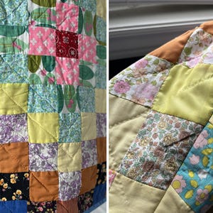 A colourful quilted jacket is displayed on a teal mannequin.  It features a patchwork design with various floral & patterned squares in shades of blue, pink, yellow, orange, and green.  Blue trim outlines the pockets and edges.
