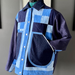 May include: A blue patchwork jacket with a collared neckline, long sleeves, and silver button fastenings. The design incorporates various blue fabric patterns, including squares and stripes, with two front pockets.
