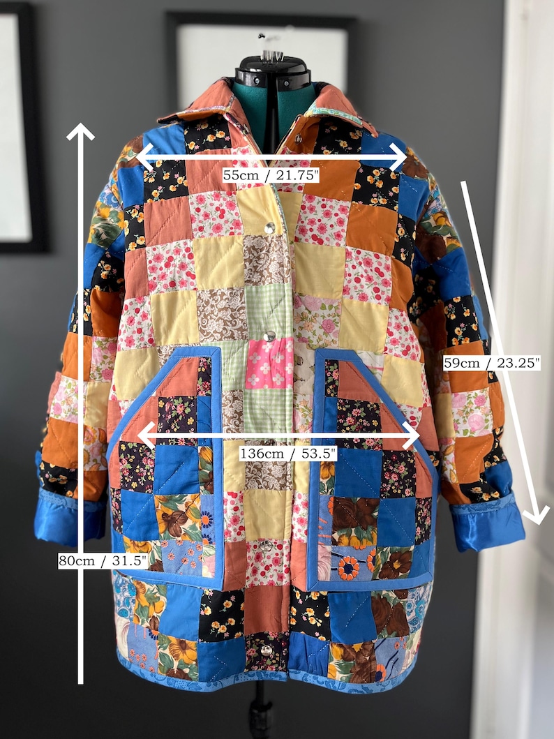 A colourful quilted jacket is displayed on a teal mannequin.  It features a patchwork design with various floral & patterned squares in shades of blue, pink, yellow, orange, and green.  Blue trim outlines the pockets and edges.