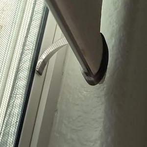 May include: A close-up view of a white window frame with a screen and a curved handle. The window is partially open, revealing a glimpse of the outside. The handle is silver and curved.