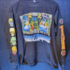 Może przedstawiać: Ciemnoszara koszulka z długim rękawem z kolorową grafiką z napisem "WHITE ZOMBIE" i "ROUTE 666". Na rękawach znajdują się twarze potworów i napis "WHITE ZOMBIE". Koszulka ma okrągły dekolt.