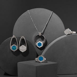 Puede incluir: Un conjunto de joyas de plata con detalles de piedras preciosas azules. El conjunto incluye un collar, un par de pendientes y un anillo. Las joyas se muestran en plataformas grises.