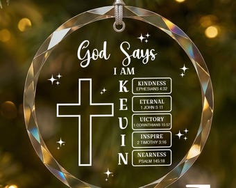 Puede incluir: Un adorno navideño de cristal circular y facetado con una cruz blanca impresa y el texto God Says I AM KEVIN, junto a palabras verticales que corresponden a versículos bíblicos como Kindness, Eternal, Victory, Inspire y Nearness.