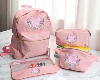 Puede incluir: Un conjunto de bolsas rosas que incluye una mochila, un estuche, una riñonera y un neceser. Cada artículo presenta un diseño de corona floral con el nombre "Sophia". El estuche contiene rotuladores de colores. El conjunto está hecho de un material ligero.