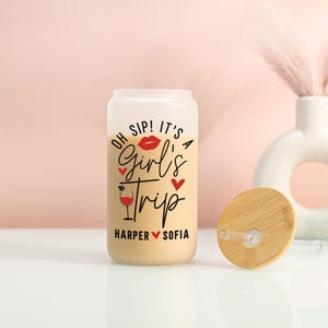 May include: A frosted glass can-shaped tumbler with a bamboo lid. The tumbler features the words "OH SIP! IT'S A Girl's Trip" in black and red script, with a red lip graphic and a wine glass illustration. The names "Harper" and "Sofia" are below.