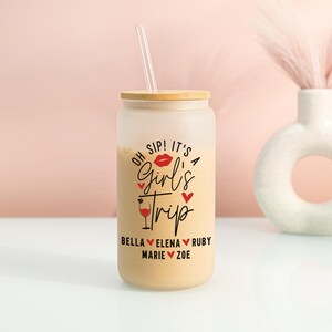 May include: A frosted glass can-shaped tumbler with a bamboo lid and a clear straw. The tumbler is filled with a light-coloured beverage and features the text "Oh Sip! It's a Girl's Trip" in black and red, with friends' names.
