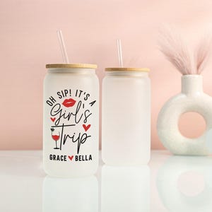 May include: Two frosted glass tumblers with bamboo lids and clear straws. One tumbler has the text "OH SIP! IT'S A Girl's Trip" in black and red, with the names Grace and Bella. The other tumbler is blank.