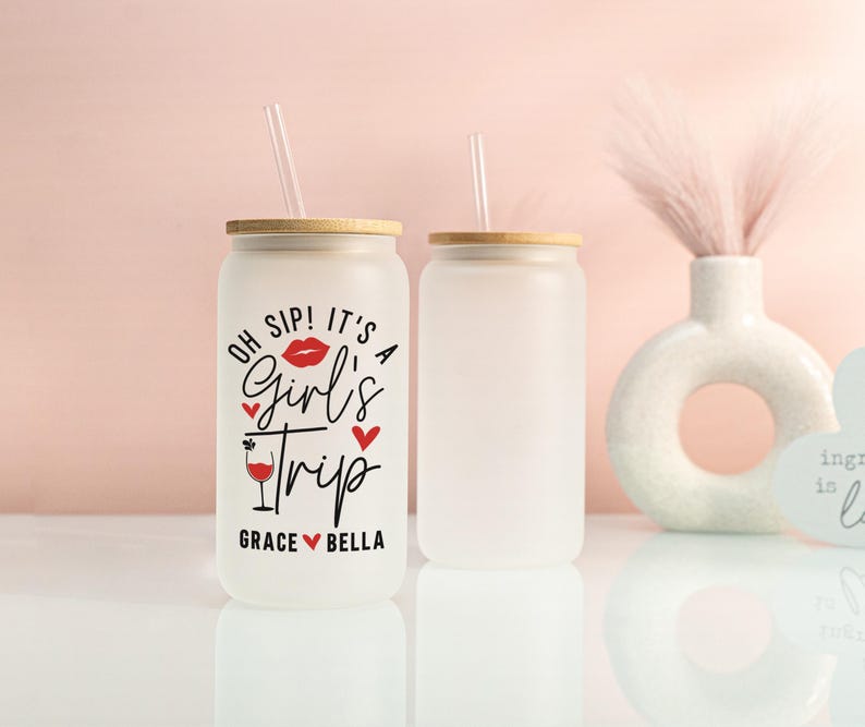 May include: Two frosted glass tumblers with bamboo lids and clear straws. One tumbler has the text "OH SIP! IT'S A Girl's Trip" in black and red, with the names Grace and Bella. The other tumbler is blank.