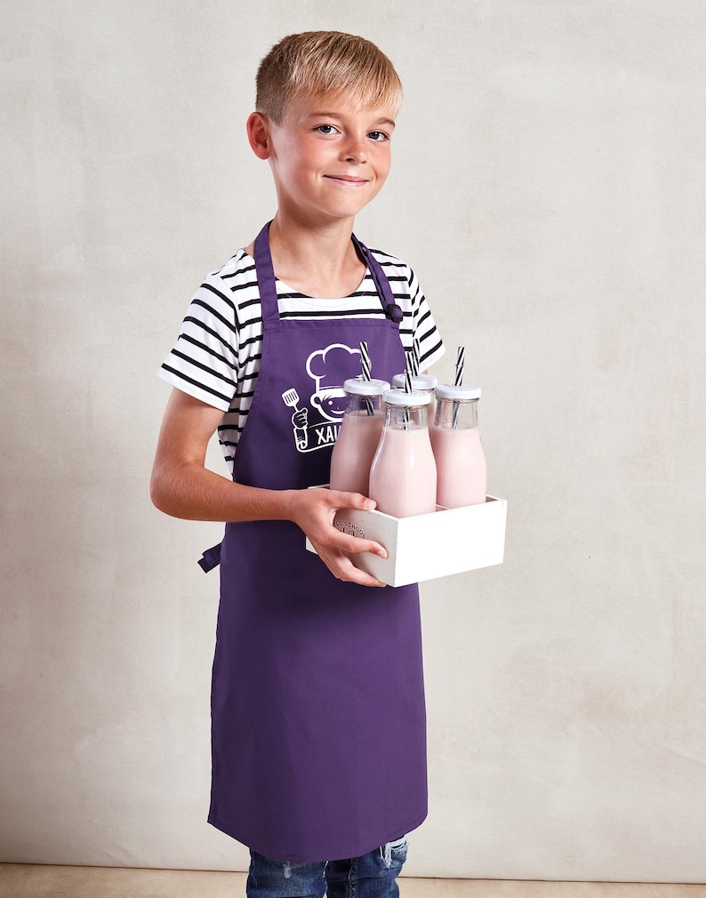 May include: A purple apron with a chef logo and text is worn by a person holding a white tray with glass bottles of pink liquid. The bottles have white lids and black and white striped straws. The person is wearing a black and white striped shirt.