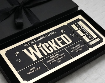 May include: A gold-colored ticket stub with the words "You are going to see... Wicked" printed on it. The ticket stub is in a black box with a black ribbon tied around it. The ticket stub also has the date "20th July 2025", a message that says "Happy Birthday Emily! Lots of love Matt xxx", and the location "Apollo Victoria Theatre".