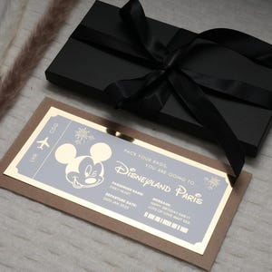 May include: A gold-colored ticket with a Mickey Mouse illustration and the text "Pack your bags, you are going to Disneyland Paris". The ticket is on a brown background.