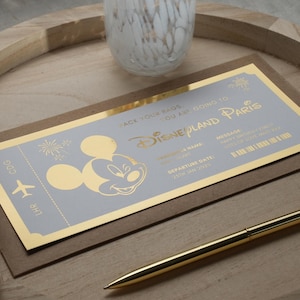 May include: A gold foil ticket with a blue background and a Mickey Mouse silhouette. The ticket says "Pack your bags, you are going to Disneyland Paris".