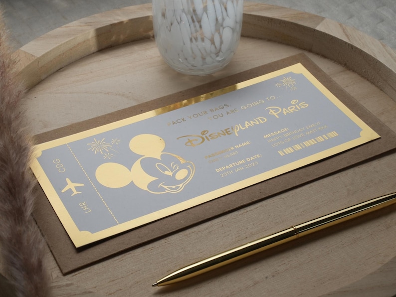 May include: A gold foil ticket with a blue background and a Mickey Mouse silhouette. The ticket says "Pack your bags, you are going to Disneyland Paris".