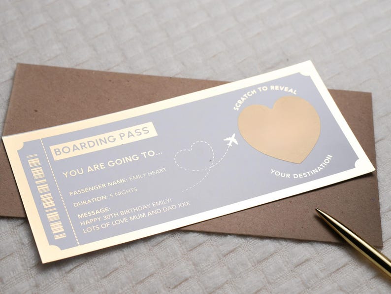Op de afbeelding: Een gouden en blauwe instapkaart met een kraslot-hart om een bestemming te onthullen. De tekst luidt "Boarding Pass You Are Going To... Passenger Name: Emily Heart Duration: 5 Nights Message: Happy 30th Birthday Emily Lots of Love Mum and Dad XXX Scratch to Reveal Your Destination"