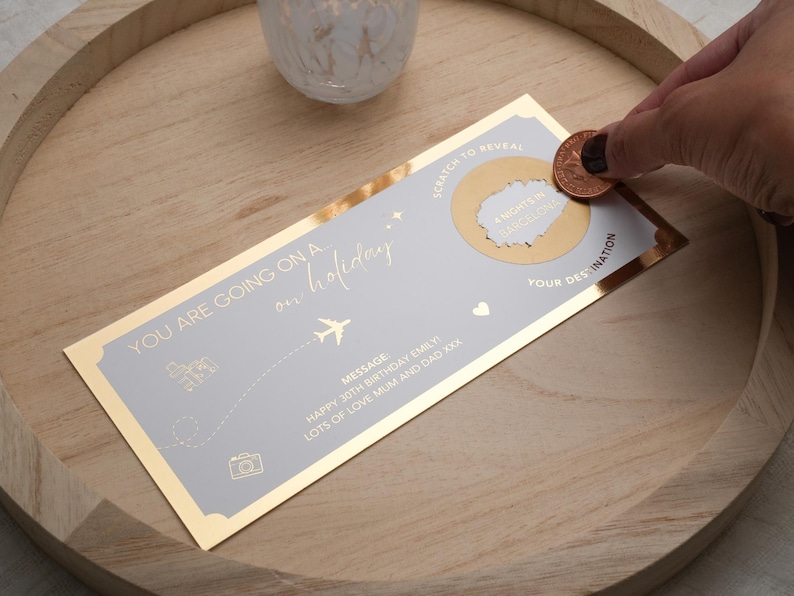 May include: A gold and gray scratch-off card with the text "You are going on a holiday" and "Scratch to reveal your destination". The card has a gold coin on top of the scratch-off area.