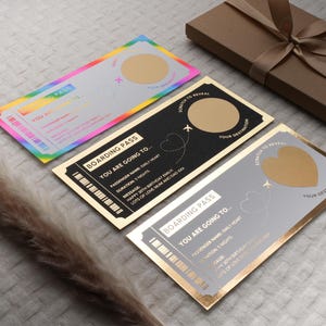 Op de afbeelding: Drie gouden boardingpassen met een krasgedeelte om een bestemming te onthullen. De bovenste pas heeft een regenboogontwerp, de middelste pas is zwart met een gouden hart en de onderste pas is grijs met een gouden hart. De tekst op de passen luidt "Boarding Pass" en "You are going to..."