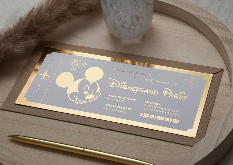 May include: A gold-trimmed invitation card with a Mickey Mouse illustration and the text "Pack your bags, you are going to Disneyland Paris". The card also includes the text "Passenger Name: Emily Heart" and "Departure Date: 25th Jan 2025".