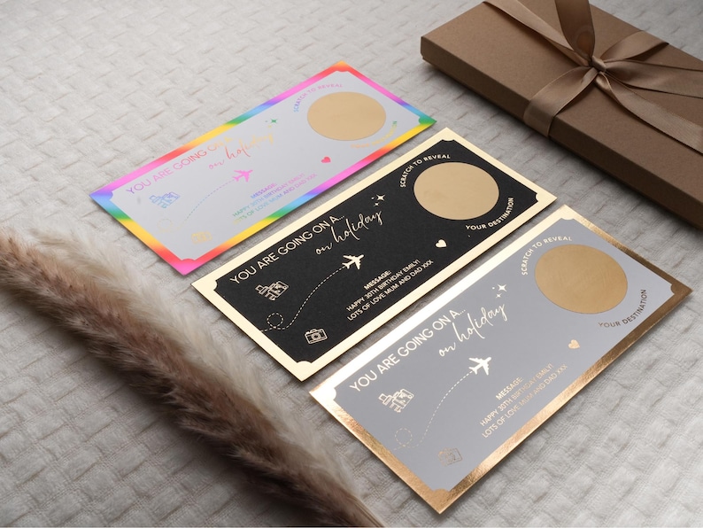 May include: Three gold foil scratch-off cards with a rainbow, black, and gray background. Each card has a gold circle to scratch off to reveal a hidden message. The text on the cards reads "You are going on a holiday".
