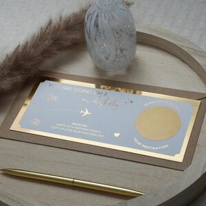 May include: A blue and gold card with the text "You are going on a holiday" and a gold scratch-off area. The card is on a wooden surface with a decorative glass object in the background.