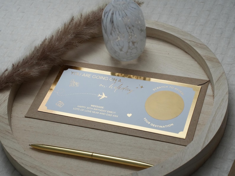 May include: A blue and gold card with the text "You are going on a holiday" and a gold scratch-off area. The card is on a wooden surface with a decorative glass object in the background.