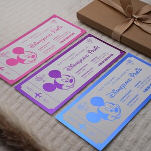 May include: Three colorful paper airplane tickets with Mickey Mouse on each. The tickets are pink, purple, and blue. The text on the tickets reads "Pack your bags, you are going to Disneyland Paris".