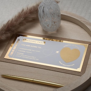 Op de afbeelding: Een gouden en witte instapkaart met een kraslot in de vorm van een hart waarop staat "Scratch to reveal your destination". De tekst op de instapkaart luidt "Boarding Pass, You are going to...", "Passenger Name:  Emily Wright", "Duration: 1 Night", "Message: Happy 30th Birthday Emily Lots of love Mum and Dad xxx".