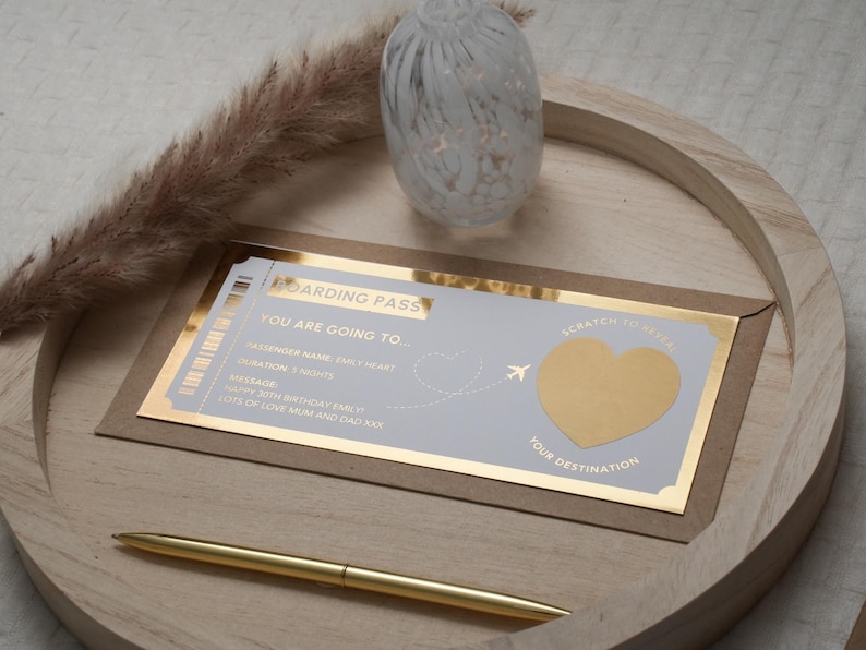 Op de afbeelding: Een gouden en witte instapkaart met een kraslot in de vorm van een hart waarop staat "Scratch to reveal your destination". De tekst op de instapkaart luidt "Boarding Pass, You are going to...", "Passenger Name:  Emily Wright", "Duration: 1 Night", "Message: Happy 30th Birthday Emily Lots of love Mum and Dad xxx".