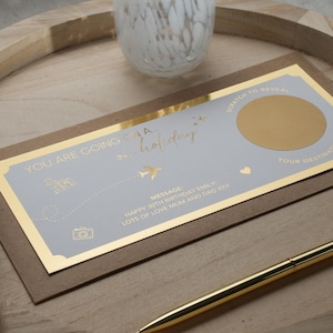 May include: A light blue and gold card with the text "YOU ARE GOING ON A HOLIDAY" and a gold circle with a scratch-off surface to reveal a hidden message. The card also includes a message that says "HAPPY 30TH BIRTHDAY EMILY LOTS OF LOVE MUM AND DAD XXX".