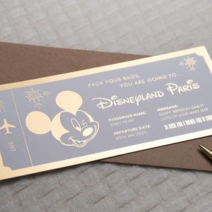 May include: A gold-colored ticket with a purple background, featuring a cartoon image of Mickey Mouse. The ticket reads "Pack your bags, you are going to... Disneyland Paris". The ticket also includes a passenger name, departure date, and a message.
