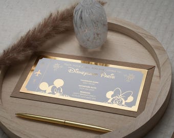 May include: A light gray invitation card with gold foil accents. The card is shaped like a boarding pass and features Mickey and Minnie Mouse. The text on the card reads "Pack your bags, you are going to Disneyland Paris".