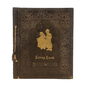 May include: A vintage brown leather-bound scrapbook with gold embossed details and a gold silhouette of two children on the front cover. The title "Scrap Book" is printed in gold lettering.