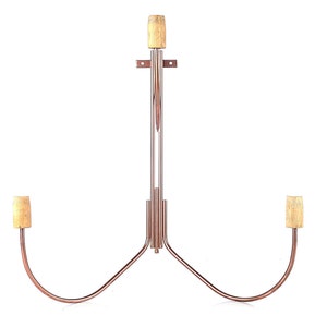 May include: A copper-colored metal wine bottle rack with three cork stoppers. The rack is shaped like a Y with two arms that curve upwards and a central arm that extends vertically.