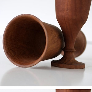 May include: Two wooden goblets with a dark brown finish. The goblets are made of wood and have a rounded base.
