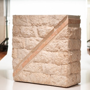 May include: A beige stone side table with a diagonal pattern of pink stone. The table is made of rough-hewn stone and has a rustic look.