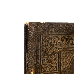 May include: Close-up of the corner of a dark brown leather-bound book with an intricate embossed floral design.