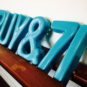 Peut inclure: Lettres en c&eacute;ramique bleue orthographiant "BUY & 71". Les lettres sont dispos&eacute;es en rang&eacute;e sur une surface en bois.