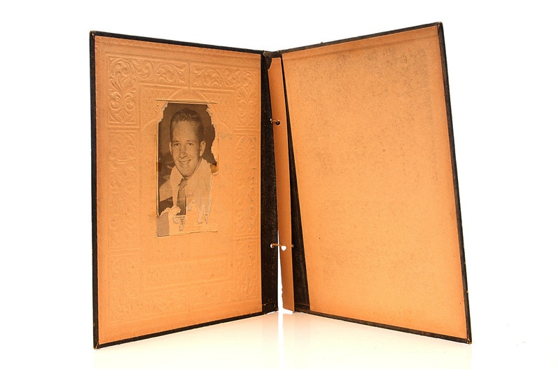 May include: An open black photo album with a black and white photo of a man in a suit and tie. The album has a decorative embossed design on the front cover.