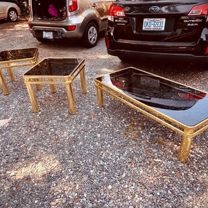 May include: Three gold-toned glass top tables with black glass tops. The largest table is rectangular and the two smaller tables are square.