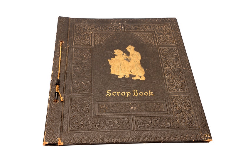May include: A vintage black scrapbook with a gold embossed design and the words "Scrap Book" on the front cover. The cover features a gold silhouette of two people.