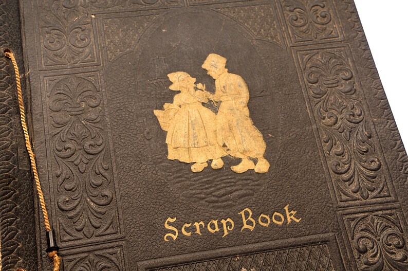 May include: A vintage brown leather scrapbook with gold embossed details and a gold inscription that reads "Scrap Book". The cover features a gold silhouette of a couple.