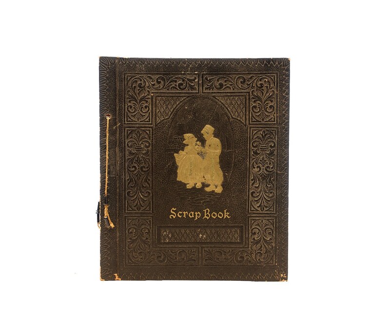 May include: A vintage brown leather-bound scrapbook with gold embossed details and a gold silhouette of two children on the front cover. The title "Scrap Book" is printed in gold lettering.