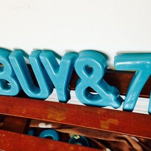Peut inclure: Lettres en plastique bleu orthographiant "BUY 871". Les lettres sont dispos&eacute;es en rang&eacute;e sur une surface en bois.