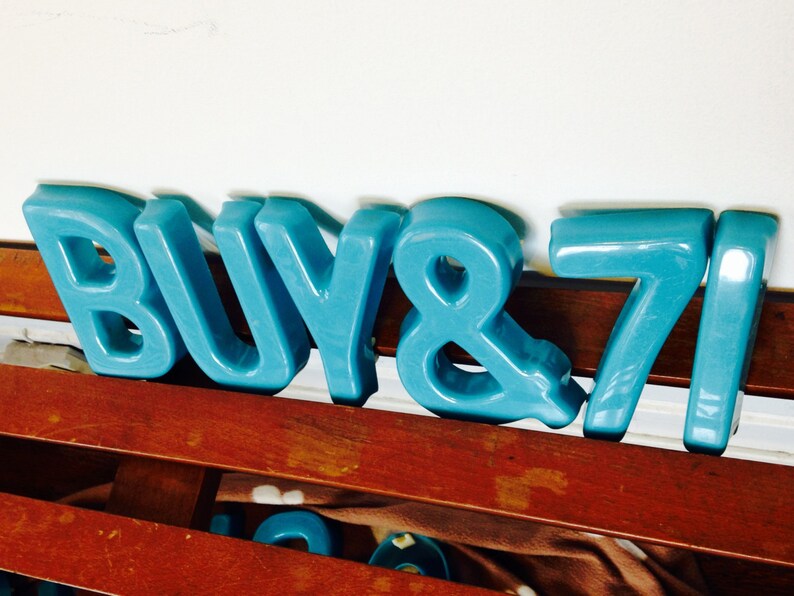 Peut inclure: Lettres en plastique bleu orthographiant "BUY 871". Les lettres sont dispos&eacute;es en rang&eacute;e sur une surface en bois.